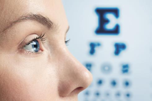 A human face seen from the side. The nose, blue eye and eyebrow are visible. In the background, letters of different sizes on the wall.