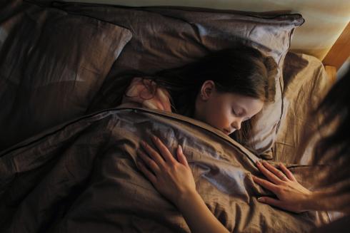 Little child sleeping in bed. Adult's hands covering the child.