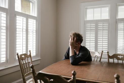 A man is sitting at a table. He leans his head on his hand and looks out of the window.