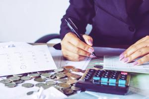 En person vid ett bord med en miniräknare, räkningar och pengar
