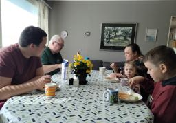 Eri-ikäisiä henkilöitä istuu ruokapöydän ääressä. 