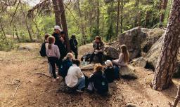 Lapsia ja aikuisia kokoontuneena metsän keskelle kalliolle.